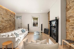 A modern living room with a stone accent wall, a white sofa, a glass coffee table, and a fireplace. - Palmer Darlinghurst - Stunning Terrace Home (Darlinghurst)