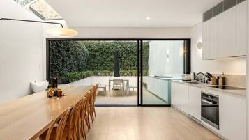 A modern kitchen with a dining area, large windows, and a view of greenery.