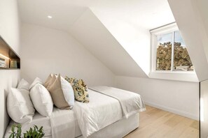 Una camera da letto con soffitto spiovente, un letto con biancheria bianca e una finestra vista alberi.