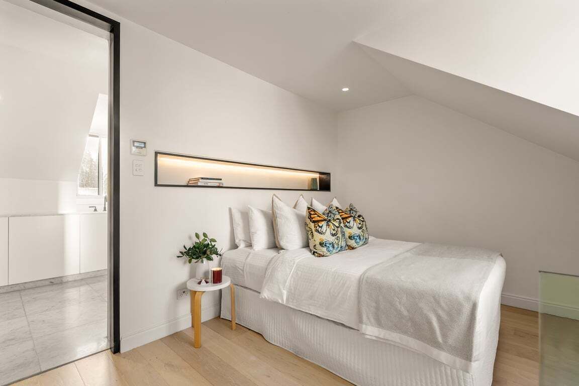 Quarto moderno com cama, mesa de cabeceira e prateleira na parede.