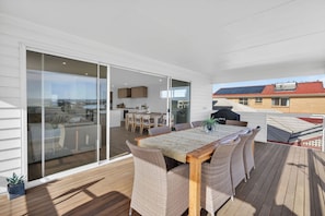 A spacious outdoor deck with a wooden table and wicker chairs, a sliding glass door leading to a balcony, and a view of the surrounding area. - Marina Breeze - Excelsior Pde (Hindmarsh Island)
