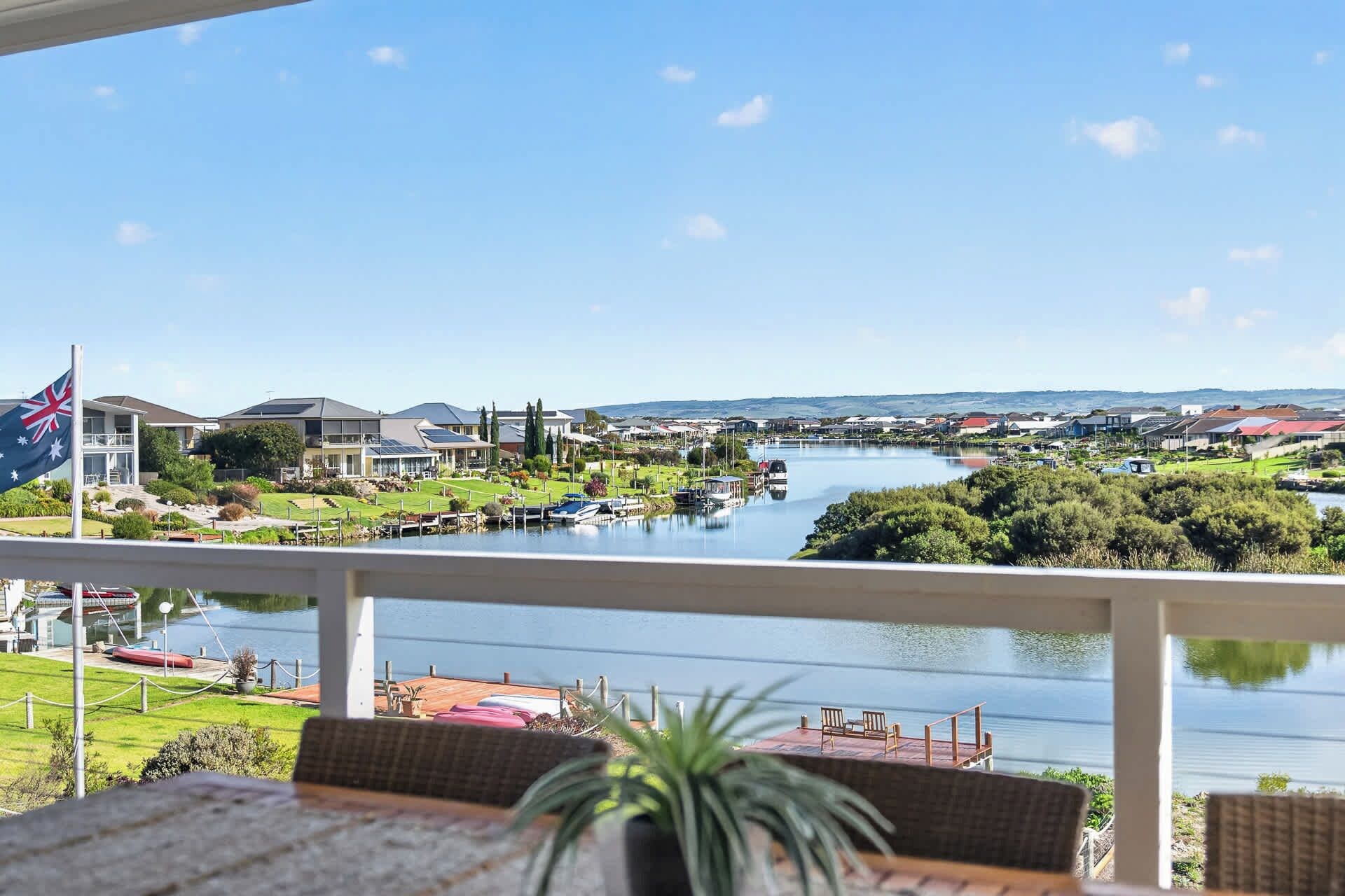 A view from a balcony overlooking a river with boats, a flag, and buildings in the distance.