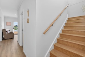 Un interior modern amb una escala de fusta, un passadís que porta a una porta i vista a una piscina a l'exterior.