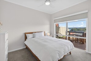 A bedroom with a bed, a nightstand, a lamp, and a view of a balcony with a table and chairs. - Marina Breeze - Excelsior Pde (Hindmarsh Island)