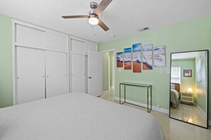 Ein Schlafzimmer mit Bett, Deckenventilator, Kleiderschrank, Nachttisch, Spiegel und Wandbildern.