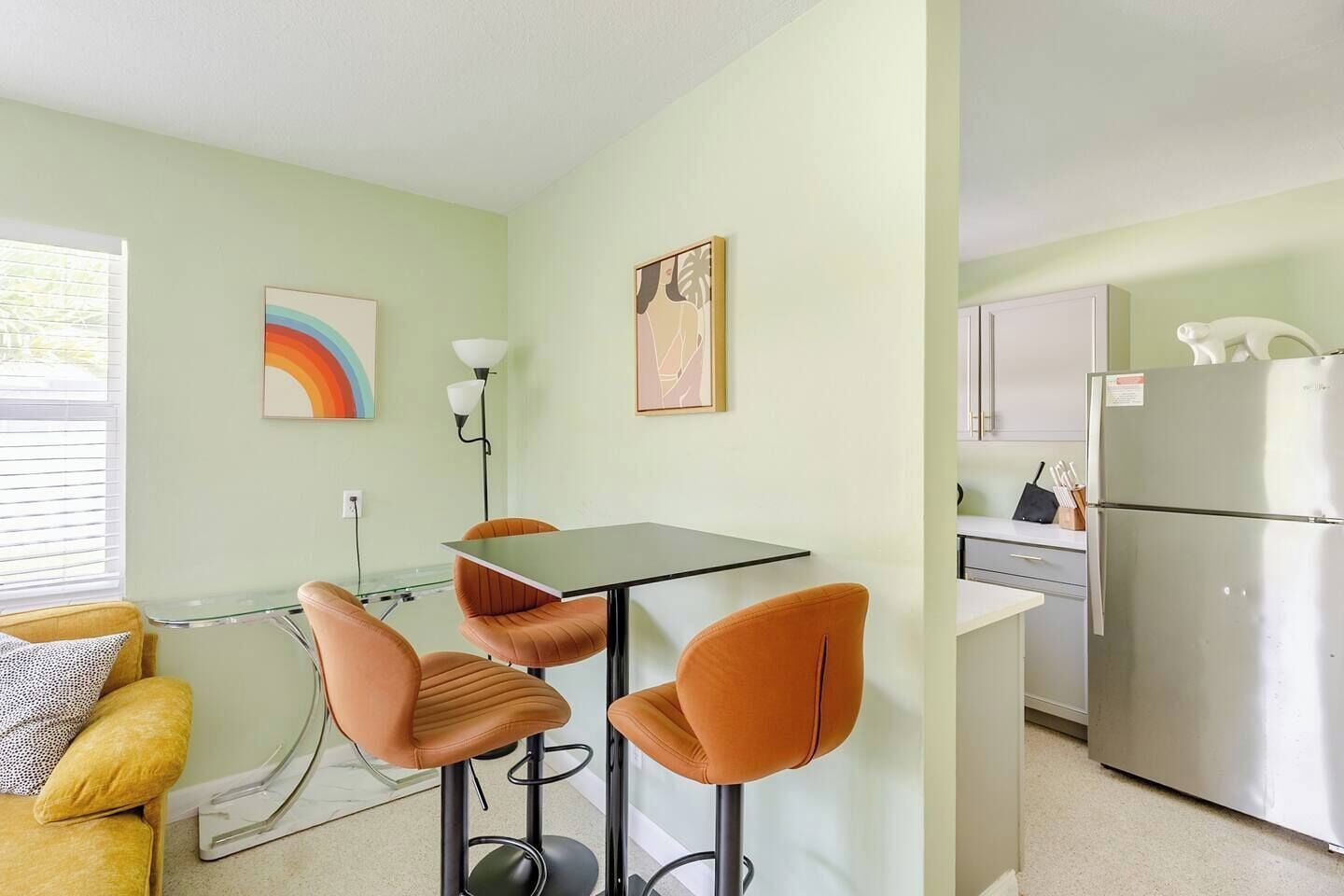 Una cocina compacta con refrigerador, una mesa de comedor con sillas y obras de arte en las paredes.