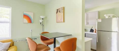 Una cocina compacta con refrigerador, una mesa de comedor con sillas y obras de arte en las paredes.