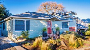 Une maison à deux étages avec une porte rouge, un porche à l’avant et un jardin bien entretenu.