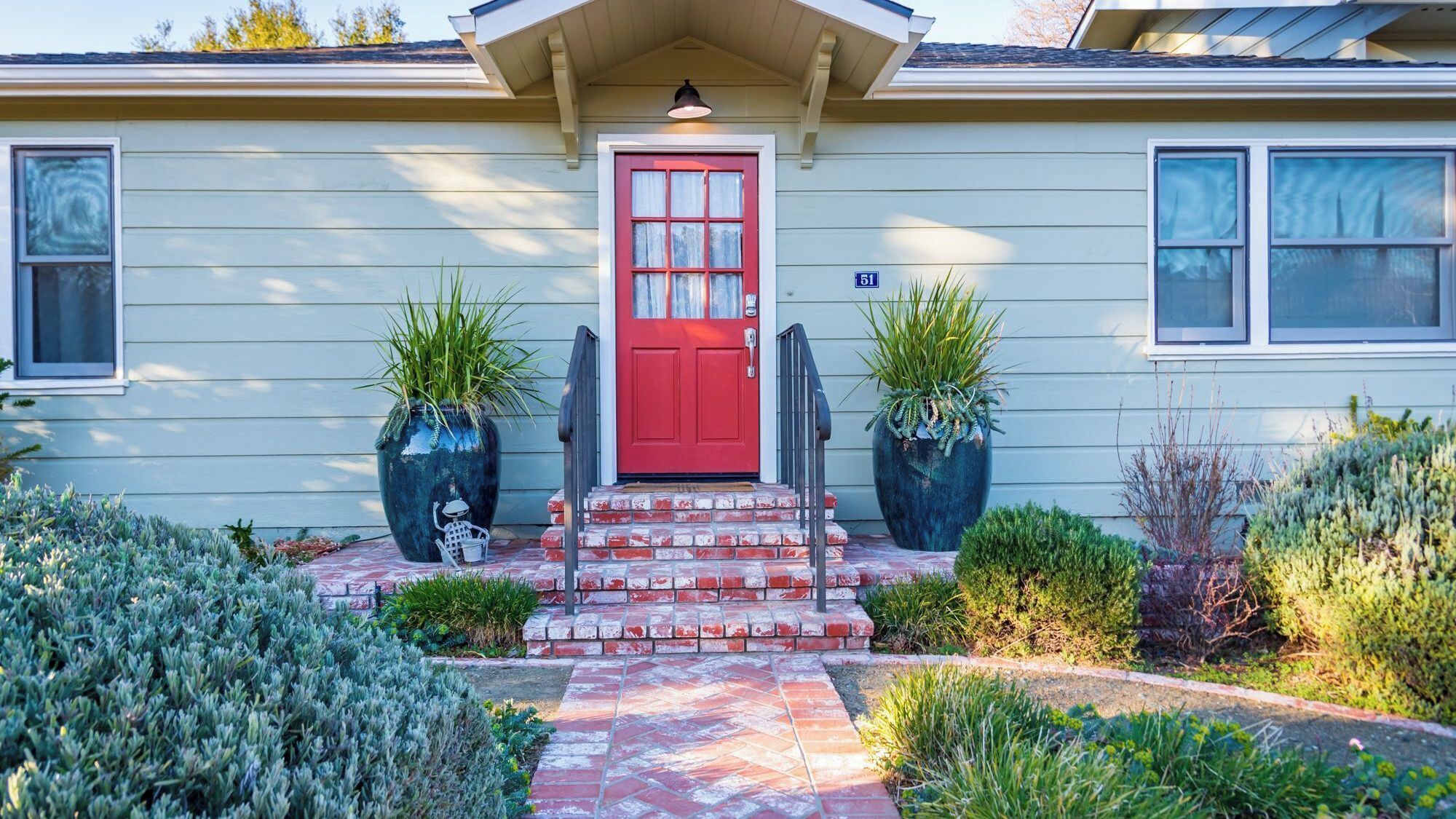 A house with a red front door, two potted plants, and a brick pathway leading to the entrance.