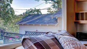 Une pièce avec un lit, une fenêtre donnant sur une maison et une étagère avec divers objets.