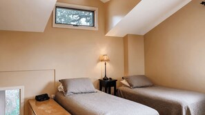 Une chambre avec deux lits simples, une table de chevet avec une lampe et une fenêtre donnant sur des arbres.