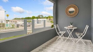 Ein Balkon mit kariertem Boden, weißen Stühlen, einem kleinen runden Tisch und einem runden Spiegel an der Wand.