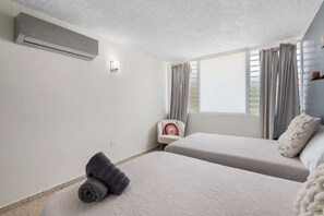 Une chambre avec deux lits, une chaise, une fenêtre avec des rideaux et un appareil de climatisation.