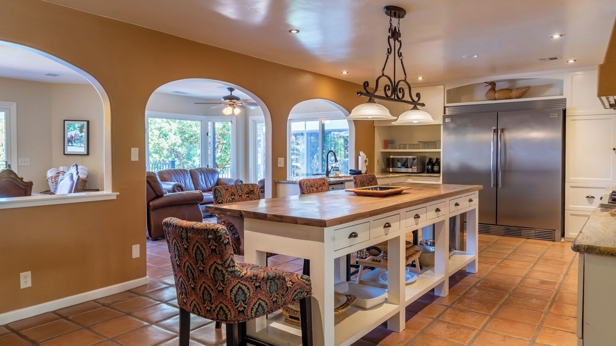 A modern kitchen with a central island, stainless steel appliances, and a dining area with patterned chairs.