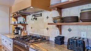 A kitchen with a gas stove, a toaster, and a coffee maker. There are shelves with plates and cups. - Merry Hill by Avantstay Pool + BBQ + Chef's Kitchen Downtown Paso Robles (Paso Robles)