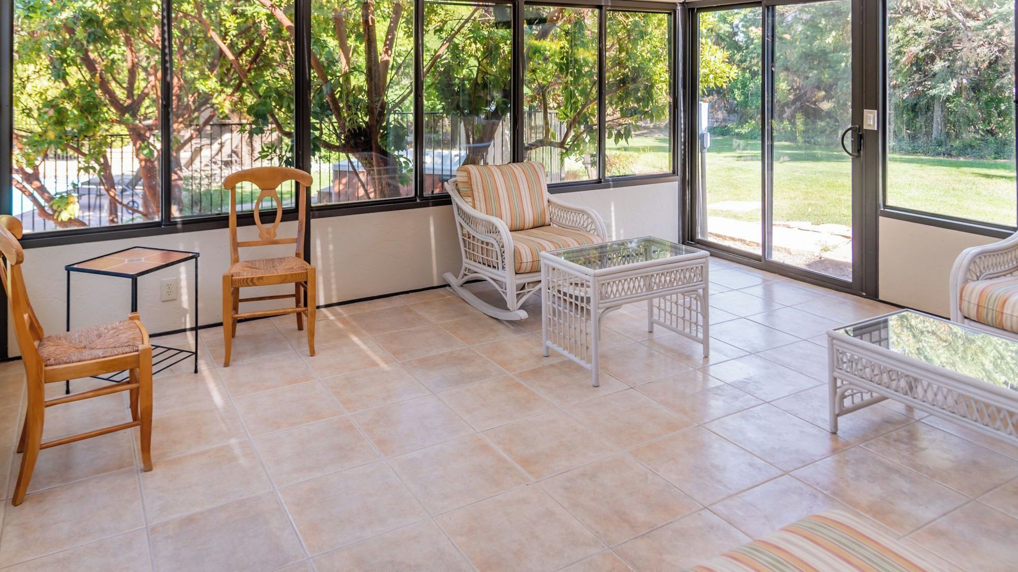 A sunlit patio with a wooden chair, a rocking chair, and a glass table.