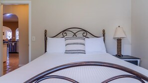 A neatly made bed with a headboard, a bedside lamp, and a view of a hallway leading to a kitchen area. - Merry Hill by Avantstay Pool + BBQ + Chef's Kitchen Downtown Paso Robles (Paso Robles)