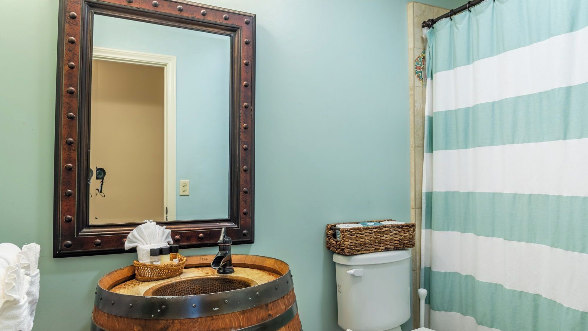 A bathroom with a wooden barrel sink, a large mirror with a decorative frame, a toilet, and a striped shower curtain.