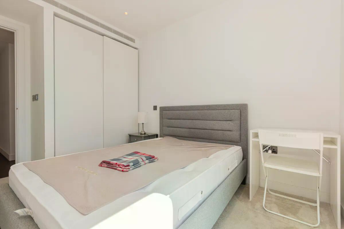 A bedroom with a bed, a bedside table, a lamp, a wardrobe, and a white shelf unit.