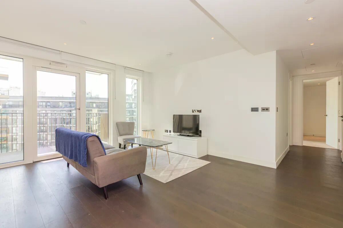 A modern living room with a sofa, a glass coffee table, and a television on a white cabinet.
