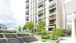 Ein mehrstöckiges Wohngebäude mit Balkonen, einem begrünten Innenhof mit Stufen zu einem Wasserspiel und einem modernen architektonischen Design.