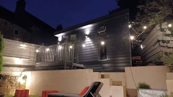 A modern two-story building with a balcony, outdoor seating, and string lights.