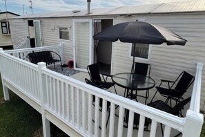 Eine überdachte Terrasse im Freien mit Tisch und Stühlen, einem schwarzen Sonnenschirm und einem weißen Geländer.