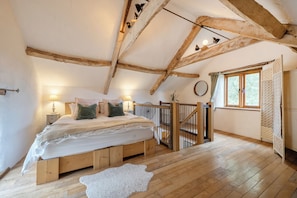 A bedroom with a wooden ceiling, a bed with pillows, a nightstand, a window with curtains, and a wooden floor.