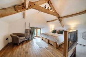 Une chambre mansardée chaleureuse avec un plafond en bois, un lit avec des oreillers, une chaise et une fenêtre avec des rideaux.