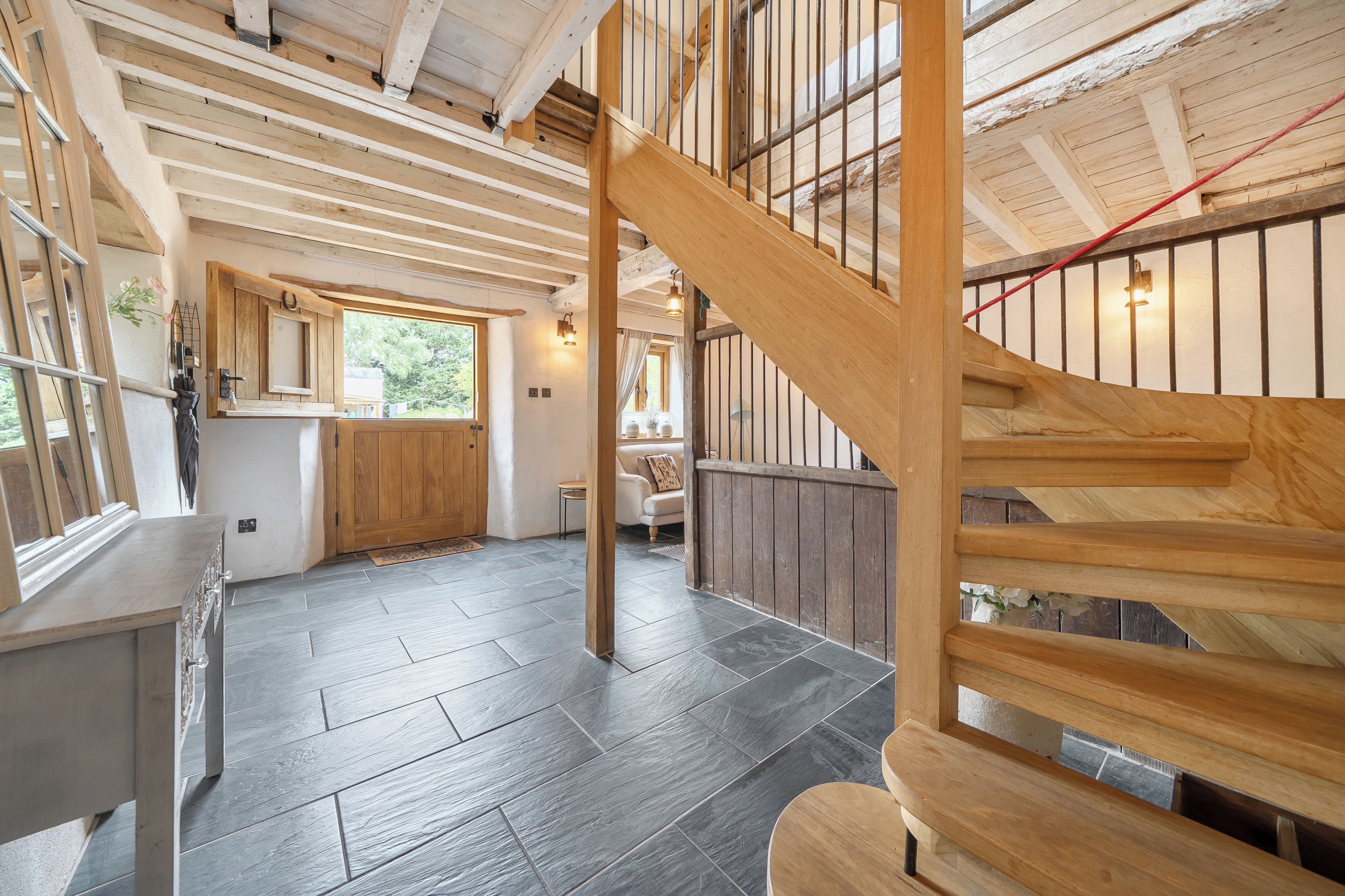 A spacious interior with a wooden staircase, a kitchen area, and a view through a window.