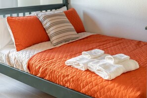 A neatly made bed with an orange quilt, white pillows, and folded white towels.