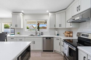 A modern kitchen with white cabinetry, a built-in dishwasher, a stove, and a window overlooking a backyard.