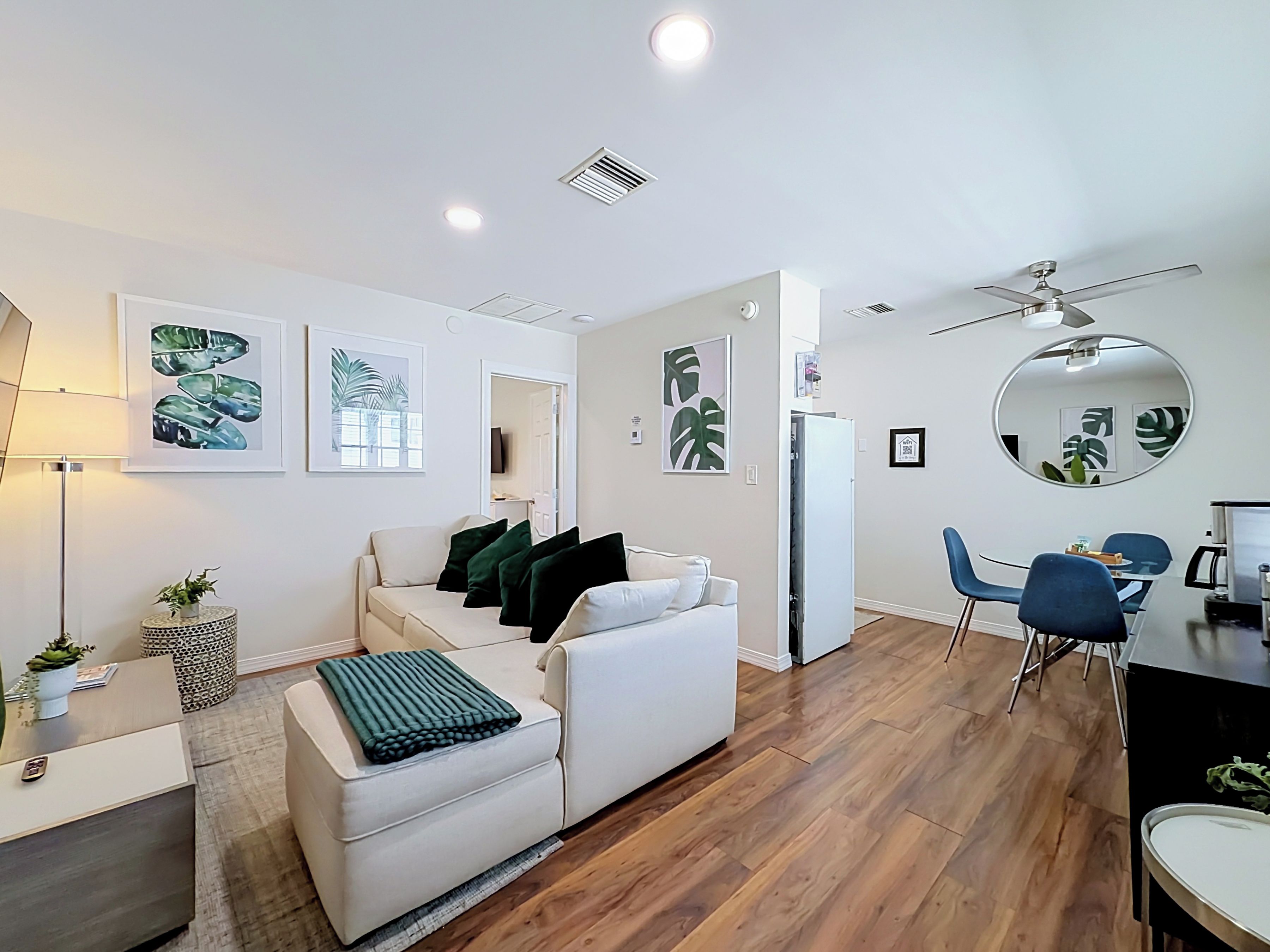 A modern living room with a white sofa, a coffee table, and a dining area with blue chairs.