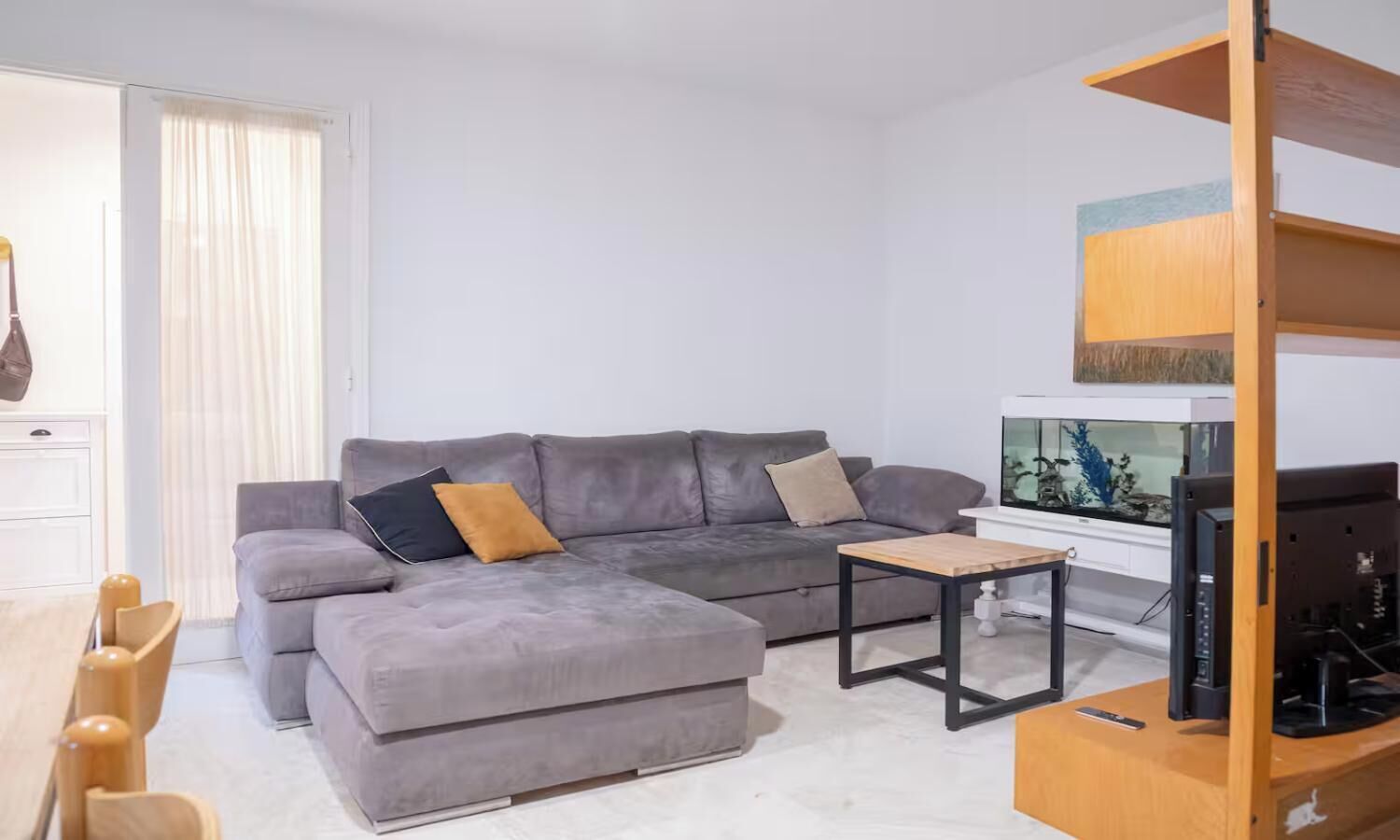 Una sala moderna con un sofá gris, una mesa de centro de madera y un televisor sobre un mueble de madera.