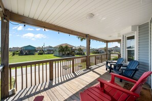 Eine überdachte Veranda mit Holzterrasse, roten Adirondack-Stühlen und Blick auf eine Wohngegend mit Häusern und einem Rasen.