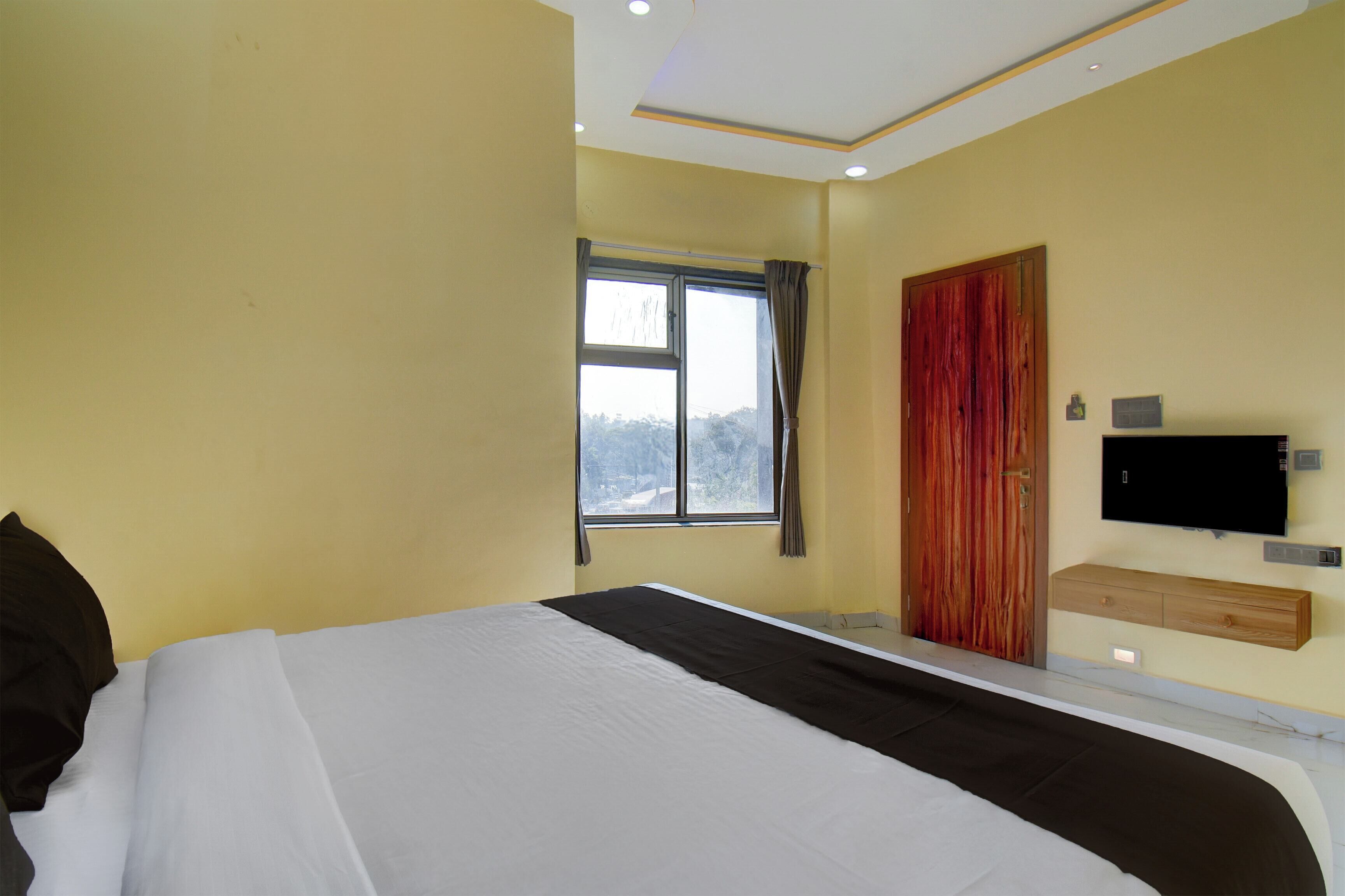 A bedroom with a bed, a window, a door, and a TV mounted on the wall.