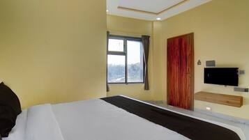 A bedroom with a bed, a window, a door, and a TV mounted on the wall.