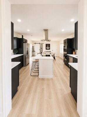 Una cocina moderna con una isla central, armarios negros y piso de madera clara.