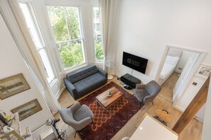 Ein modernes Wohnzimmer mit einer Couch, zwei Sesseln, einem Couchtisch und einem Flachbildfernseher.