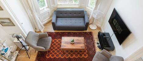 A living room with a sofa, two armchairs, a coffee table, a TV, and a large window.