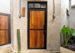 Uma porta de madeira com moldura preta, uma placa na parede e um vaso com planta.
