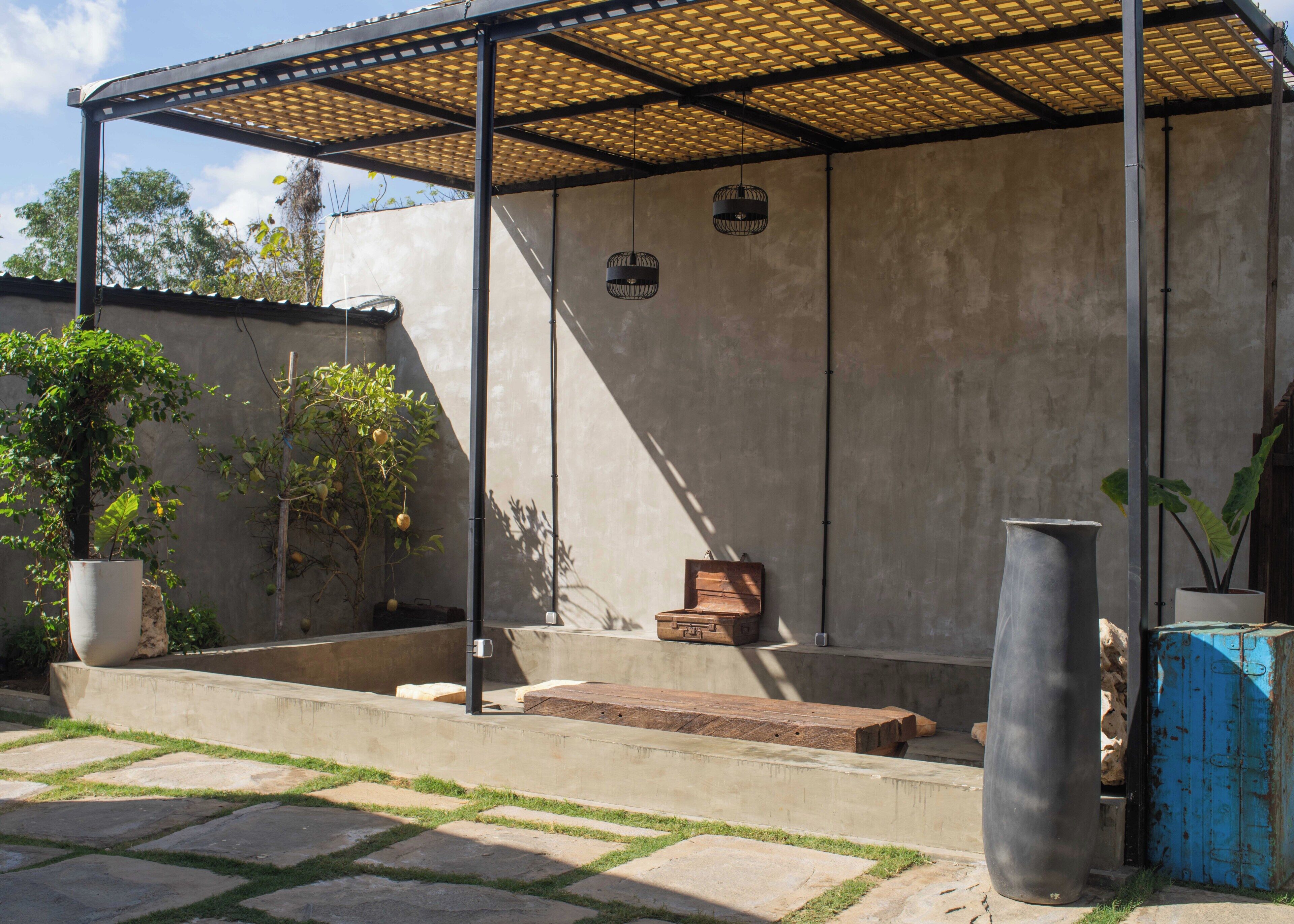Un área de estar al aire libre techada con pared de hormigón, plantas en macetas y una jardinera grande.