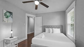 A bedroom with a bed, a nightstand, a ceiling fan, a door, and a window.