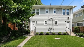 A two-story residential building with a front yard, a wooden fence, and a clear sky.