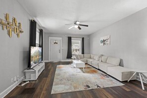 A modern living room with a sectional sofa, a flat-screen TV, and a ceiling fan.