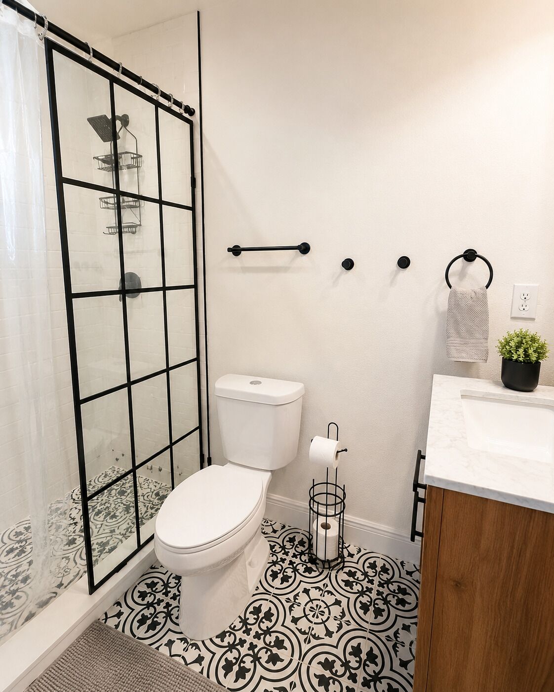 A bathroom with a glass-enclosed shower, a toilet, a sink with a marble countertop, and a patterned floor.