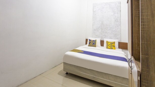 Un lit simple avec un matelas blanc, une couvre-lit bleue et jaune, et deux oreillers à motifs géométriques.