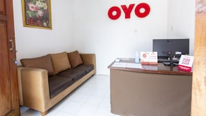 Un espace d’accueil avec un canapé marron, un bureau avec un ordinateur et un panneau fixé au mur sur lequel on peut lire « OYO ».