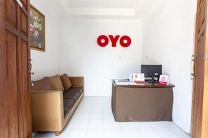 A room with a brown sofa, a desk with a computer and some items, and a wall with a large red 'OYO' sign.