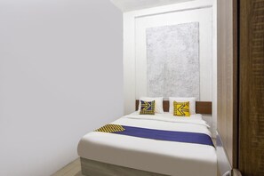 A bed with a white mattress, a blue and yellow bedspread, and two pillows with geometric patterns.